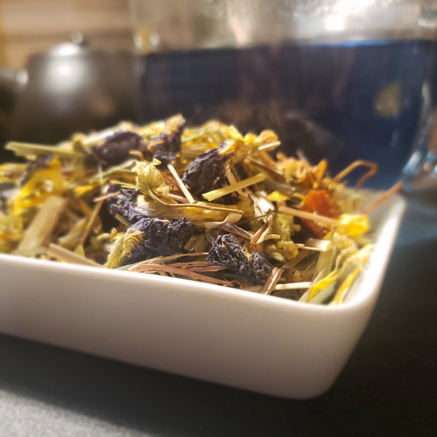 Image of loose leaf tea and glass tea cup with blue tinted tea in the background.